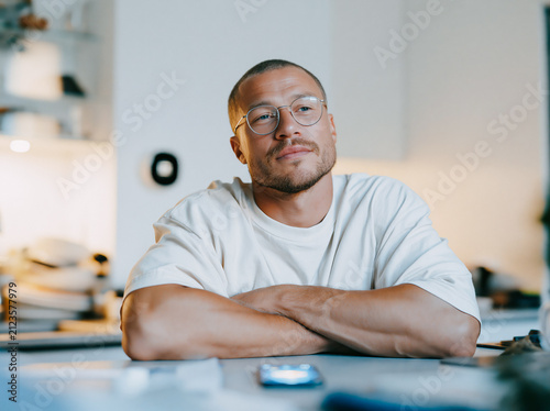 Thoughtful Young Man with Glasses Sitting with Arms Crossed in Bright Modern Office