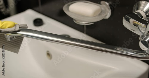 Cleaning the bathroom faucet, hands in yellow gloves wipe the faucet with a cleaning solution.