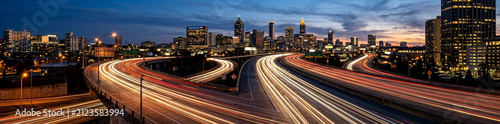 Long exposure city traffic at dusk with light trails. Urban night highway with motion blur car lights and skyscrapers.