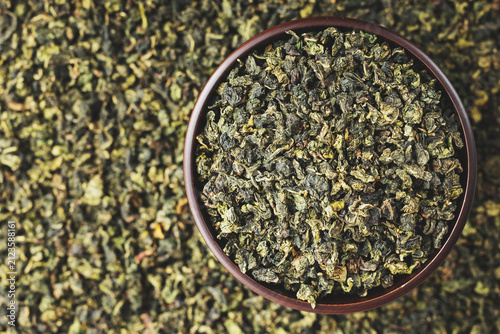 Dark wood bowl overflowing with Tie Guan Yin on full tea background