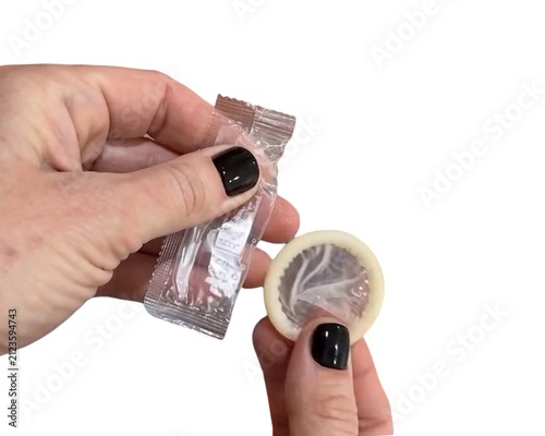 A person with black nail polish opening a silver condom wrapper and holding an unwrapped latex condom against a white background.