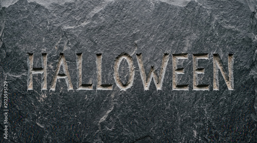 Fototapeta premium Carved word halloween displayed on a rough dark stone surface. The textured rock background creates a spooky and mysterious seasonal atmosphere.