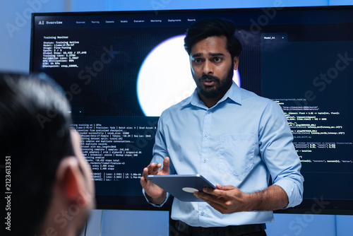 Indian male Software Engineer, Developer working with Team, Looking at Monitoring, Presenting coding, data, AI Machine Learning Model to Colleague, Discussion, Reviewing and Brainstorming together.