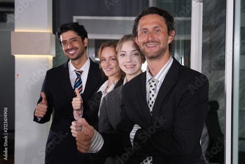 Obraz na płótnie A quiet chuckle escapes the bearded businessman in front as the team holds its final thumbs up pose, four confident happy faces filling the tight close frame completely