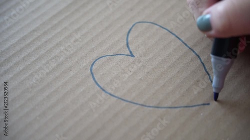 Hand drawing a heart with a blue highlighter on cardboard, representing love, warmth, or simple emotional expression, close-up