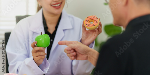 Nutritionist presenting green apple and donut for healthy food choice during patient consultation
