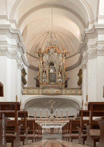 Symmetrical interior of Saint Augustine Convent church in Matera, Italy. Ornate organ, crucifix altar, and wooden pews under vaulted ceilings in historic Basilicata.