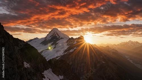 Sunburst over snowy mountain peaks under a dramatic orange sunset sky