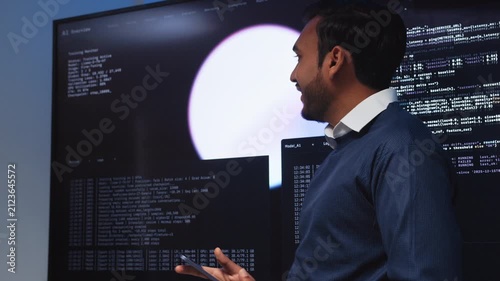 Professional Indian Male Software Engineer Collaborating with team in Tech Office, Looking and Pointing to Coding, AI Model and Data on Screen, Reviewing, Presenting Information to team in Office.