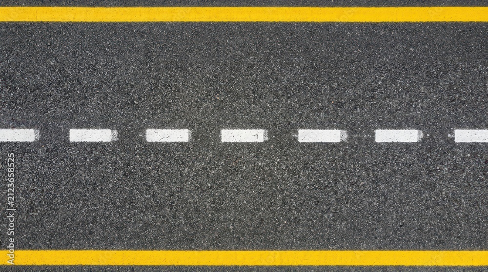 Fototapeta premium Detailed high angle view of textured asphalt road surface with solid yellow edge lines and white dashed markings, providing a clean background for transport and infrastructure projects or