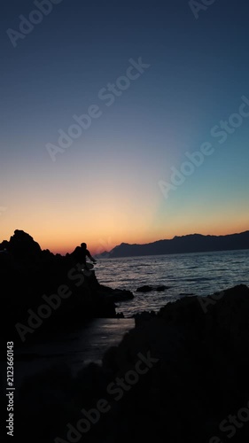 Vertical screen Sunset fishing silhouette on rocky Adriatic coast captures peaceful evening solitude calm sea horizon and mindful travel moments after a warm summer day