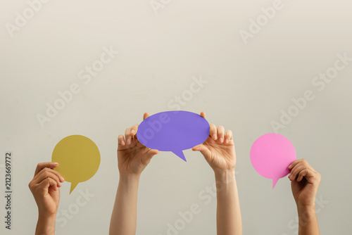 Raised hands hold colorful speech bubbles against a plain background