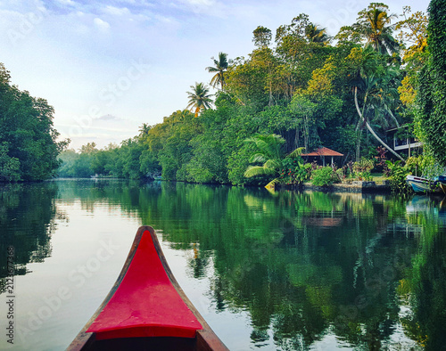 Obraz na plátně Peaceful Sri Lankan river canal with a red canoe bow, lush tropical banks, and m