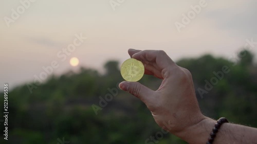 Hand holding a gold Bitcoin coin with a glowing sunset in the background, illustrating cryptocurrency investment, blockchain innovation, digital assets, and modern financial technology.