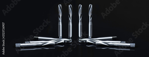 Symmetrical arrangement of precision spiral flute thread taps on black background with reflection. Industrial CNC metalworking tools set for machining.