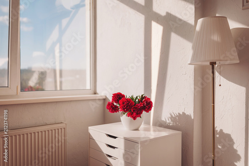 Sunlight dances through the window, illuminating a vase of red flowers in a cozy room setting