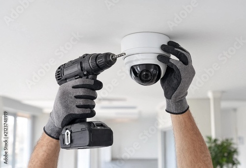 Professional technician installs modern dome security camera using cordless drill on office ceiling, highlighting surveillance, workplace safety, commercial security, precision installation, and tech.
