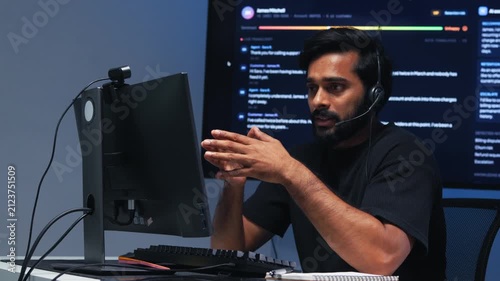Focused Indian Male IT Customer Service Agent Communicating with Client for Computer Issue, Remote IT Assistance, Live Communication and Technical Problem Resolution at desk in call center office.