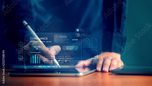 Compliance audit trail system for risk monitoring and regulation. Businessman using stylus pen on tablet with virtual compliance dashboard showing risk score and audit status.