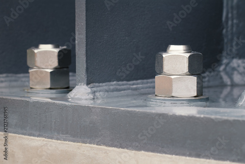 close-up of high-strength steel anchor bolts and heavy hex nuts fastening structural steel column to concrete foundation, steel construction, structural engineering, infrastructure, building assembly