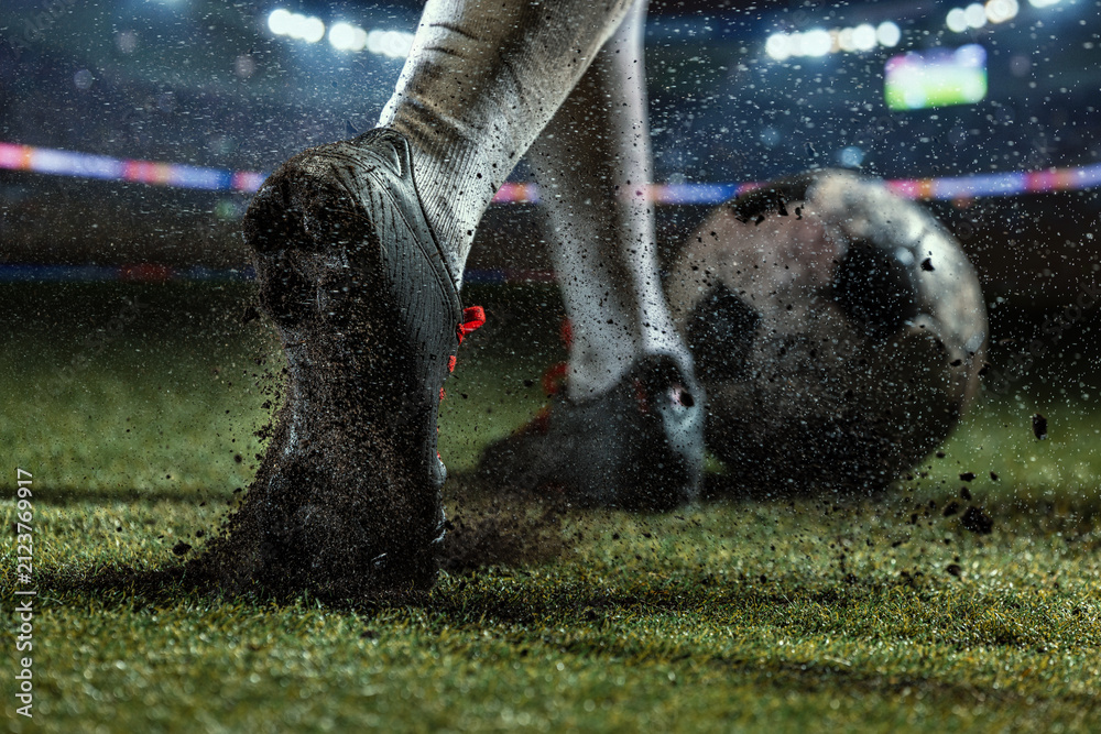 Fototapeta premium Macro view of mud-caked football studs digging into wet turf beside spinning soccer ball. Concept of traction and grip, rainy match action, durable footwear advertising.
