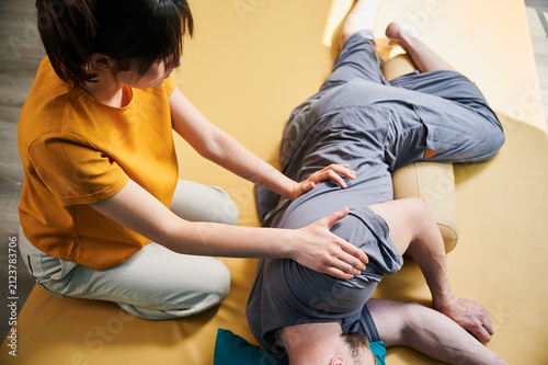 Masseuse making thai yoga massage. Woman therapist doing traditional massage treatment for male patient indoors. Client lying on mat, meditating, enjoying hand massage in calm atmosphere.