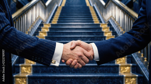 Two men in elegant suits close a business deal with a firm handshake on a luxurious marble staircase. Corporate partnership, agreement, and trust between professional executives seal a successful