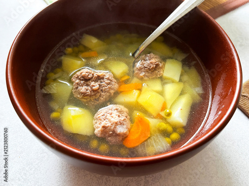 A Ceramic Bowl of Soup with Meatballs, Green Peas and other Vegetables on White Tablecloth. Traditional Slavic Dish. Homemade Food.