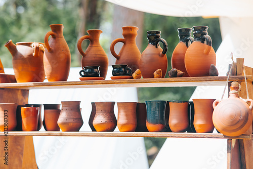 Clay pottery items are arranged neatly on wooden shelves at a medieval festival. These pieces represent the craftsmanship and daily life of people during the Middle Ages