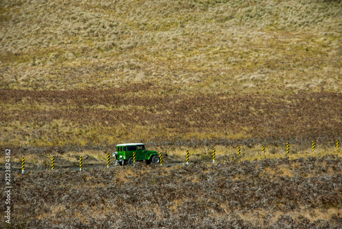 Bright green vintage off-road vehicle driving across the rugged grassy landscape of the Bromo Caldera. Iconic volcanic scenery in East Java, Indonesia.