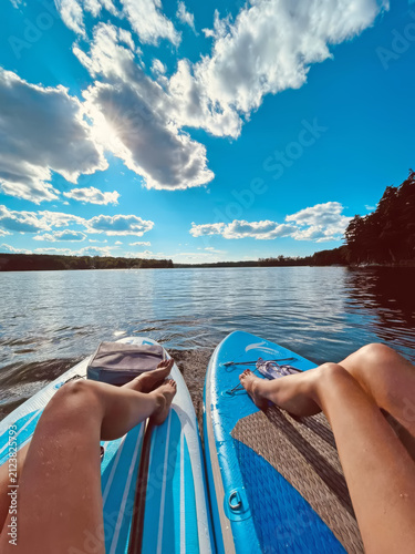 Two people relaxing on paddleboards on a calm lake under a blue sky