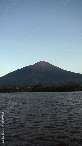Majestic view of Mount Cikuray in Garut with a calm lake water surface in the afternoon.	