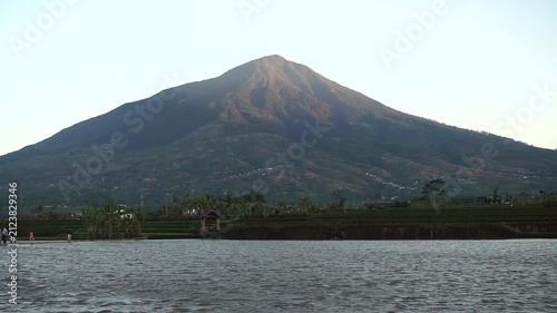 Majestic view of Mount Cikuray in Garut with a calm lake water surface in the afternoon.	