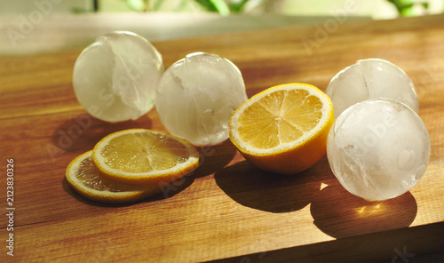Lemons and ice cubes on a wooden board, top view. Preparing to make lemonade, chilled with ice cubes. Melting ice, lemon slices. Refreshing drinks. Food backgrounds, daylight, sun reflections