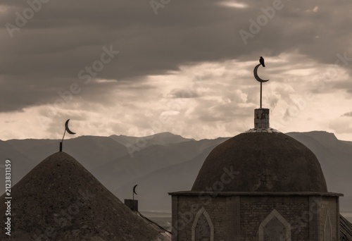 Obraz na plátně Ancient Islamic domes with crescent moon symbols against a background of dramatic mountain ridges and overcast sky