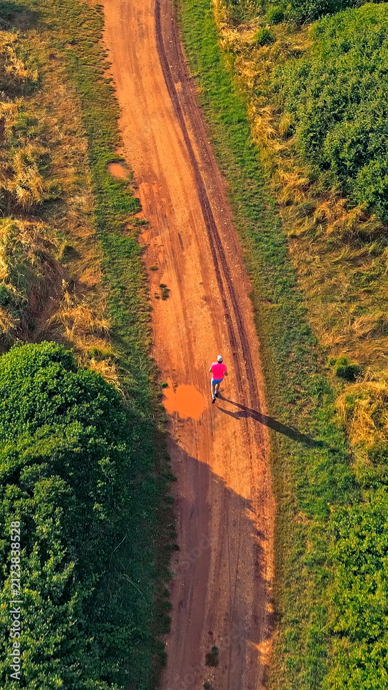 Obraz premium A senior adult jogs along a dirt path surrounded by lush greenery, highlighting their dedication to a healthy lifestyle in a serene natural setting.