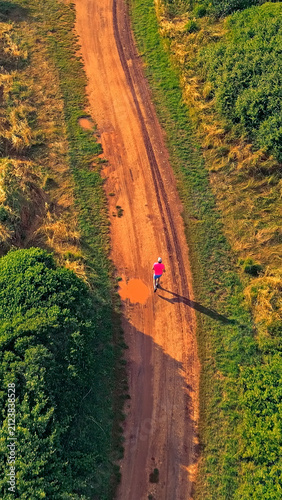 A senior adult jogs along a dirt path surrounded by lush greenery, highlighting their dedication to a healthy lifestyle in a serene natural setting.