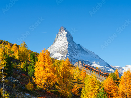 Passenger train on a railway in Zermatt, Switzerland. Autumn nature in the Alps. Train passes through autumn forest with Matterhorn peak in background.