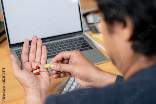 A male office worker taking painkiller medication while sitting at his desk in a modern office environment.
