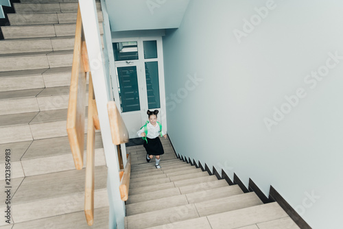 Bild auf Leinwand Young schoolgirl running up stairway with green backpack in school corridor, exc