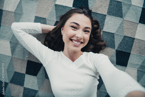 Cuadro en lienzo Smiling young woman lying on a patterned rug taking a selfie, relaxed and happy