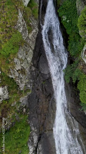 Vertical drone flight over mountain waterfall and dramatic landscape at sunset