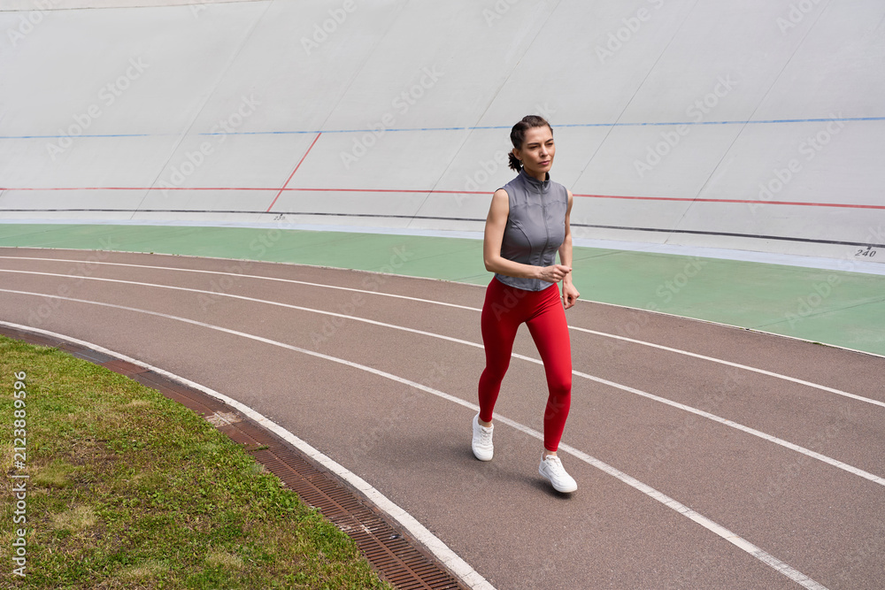 Fototapeta premium Sporty woman joyfully jogging on a running track surrounded by green grass at daytime