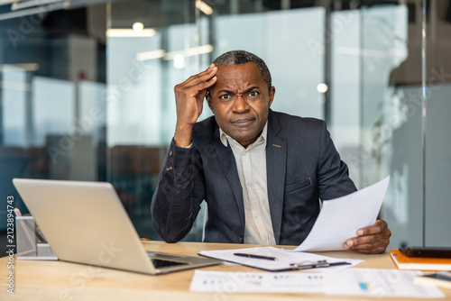 Foto Mature adult businessman experiencing a headache and confusion, trying to compre
