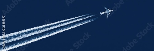 A jetliner ascends into a deep blue sky, leaving behind three distinct vapor trails