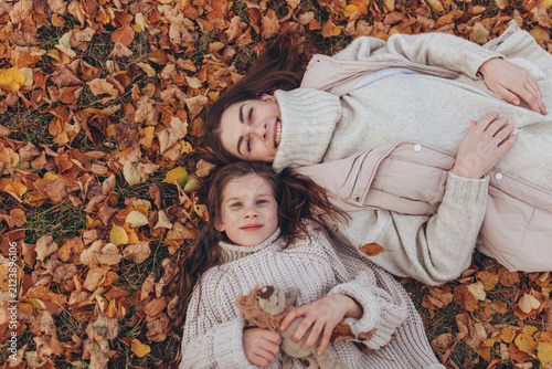 Canvas Print Top view of mother and daughter lying on fallen autumn leaves in park