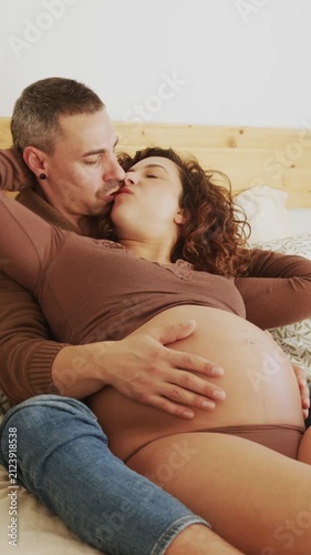 Pregnant Latin couple cuddling and caressing belly in bed