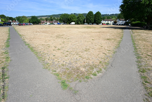 Diverging footpaths in front of a dry arid village green during the heatwave of August 3rd 2026. 