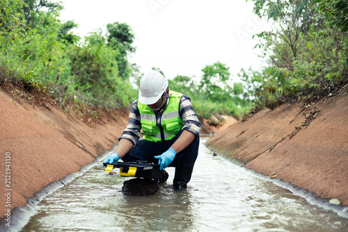Water quality inspection in agricultural irrigation canal by environmental engineer collecting water samples.