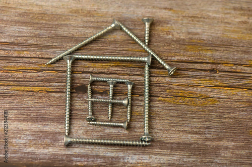 Fotografía Creative construction of a house shape using silver screws on rustic wooden back